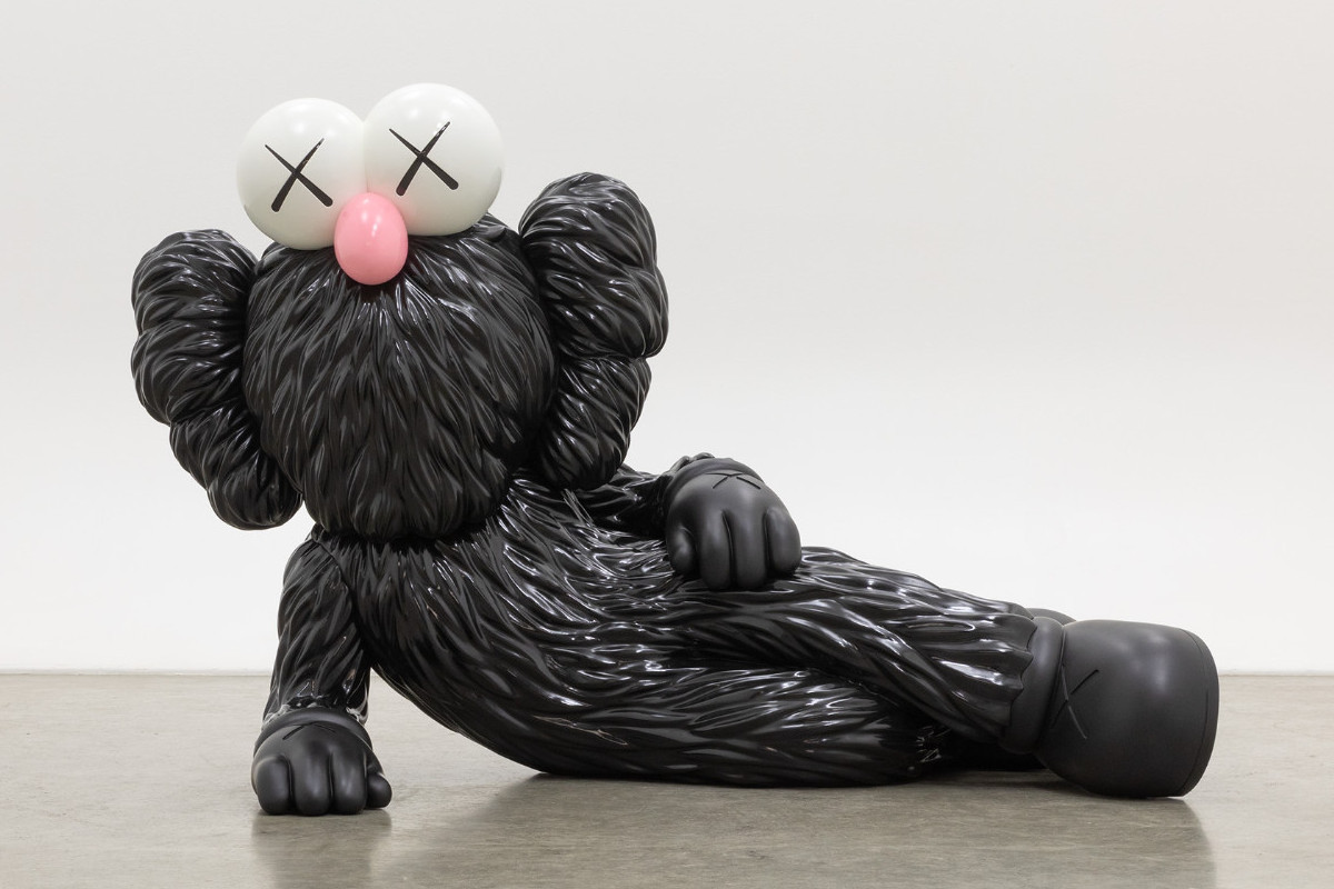 Skulptur einer seitlich aufgestützt, liegenden, schwarz pelzigen Comicfigur mit einer pinken Stupsnase und X-Augen. KAWS | TIME OFF, 2021 | Privatsammlung © KAWS | Foto: courtesy KAWS Studio