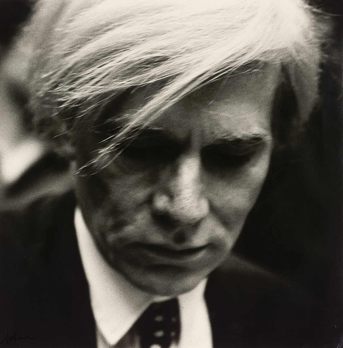 Portrait photography of Andy Warhol looking down.