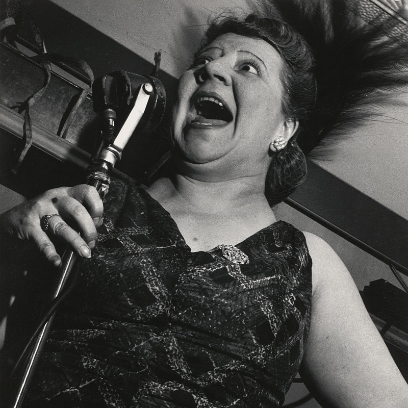Eine Frau im Abendkleid, die ein Stehmikrofon zum Gesicht hält. Ihr Mund ist dabei weit geöffnet. Credit: Lisette Model | Sängerin im Cafe Metropole, New York City, 1946 | ALBERTINA Wien © 2025 Estate of Lisette Model, courtesy Lebon, Paris / Keitelman, Brussels