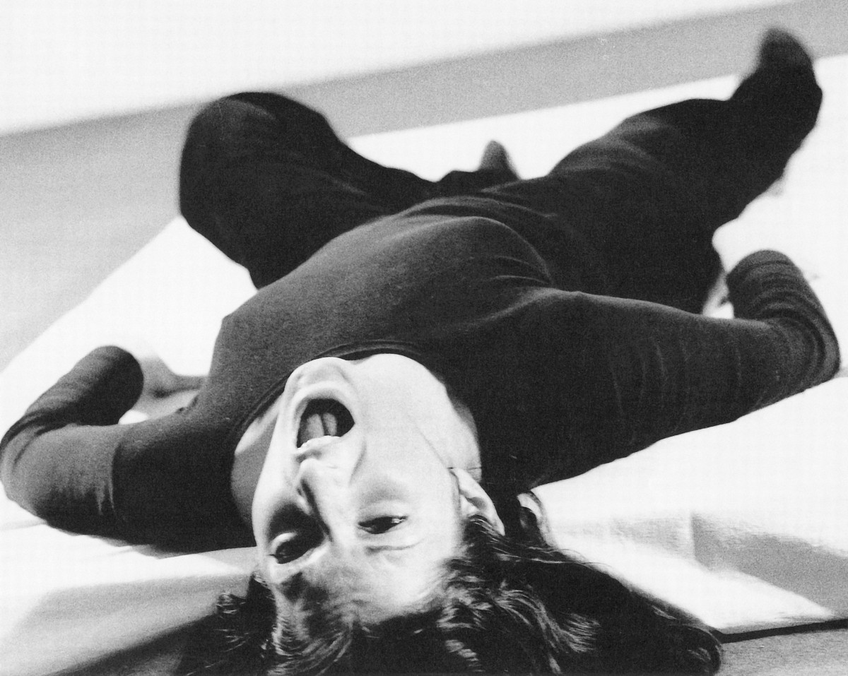 Marina Abramović lies on her back with her head bent back and screams continuously; her body seems tense.