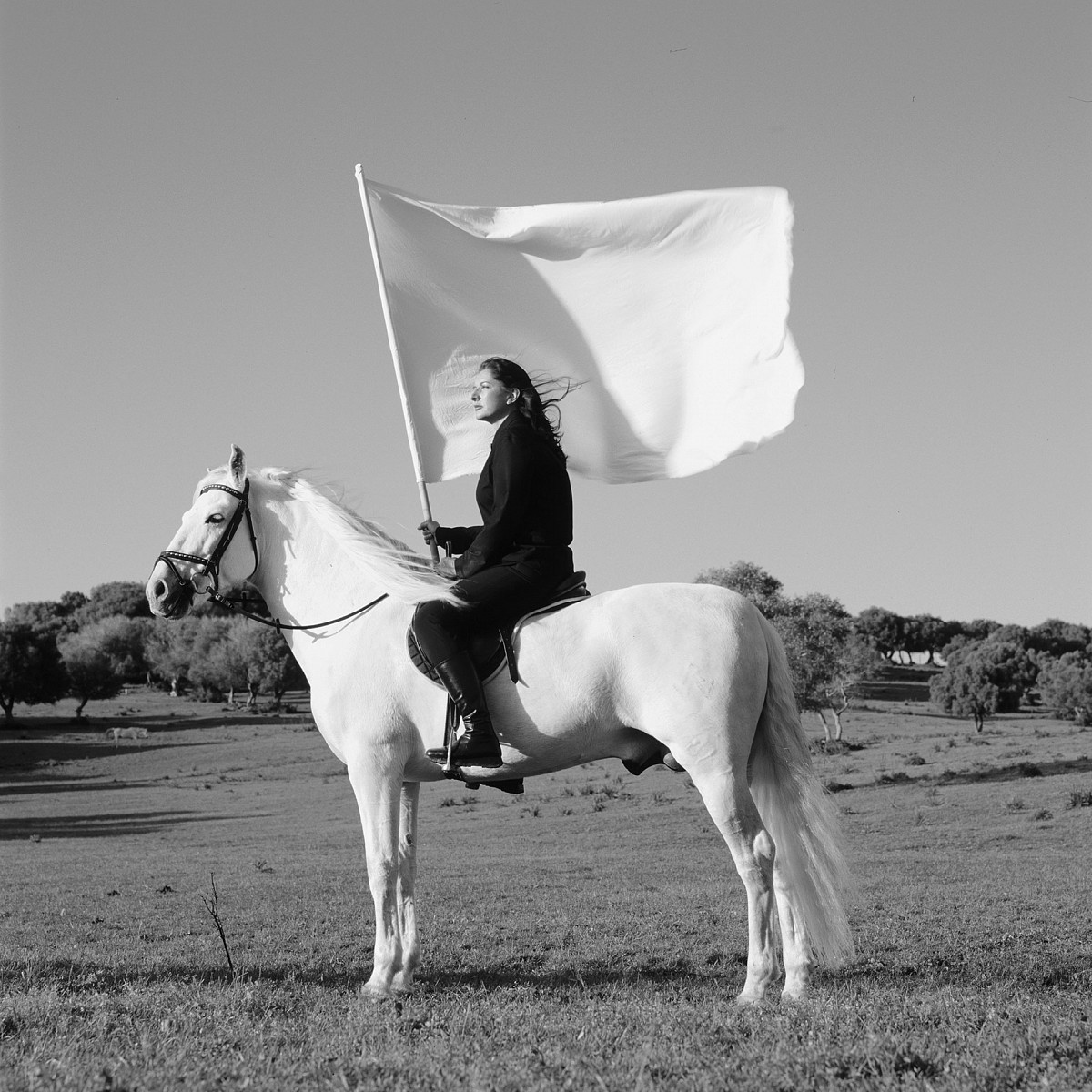 Schwarz-Weiß-Fotografie, auf der die Künstlerin auf einem weißen Pferd sitzt und eine große weiße Fahne hält.