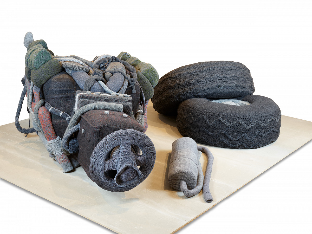 Ein Automotor, zwei Autoreifen übereiandergestapelt und ein Auspuff. Alles gehäkelt.