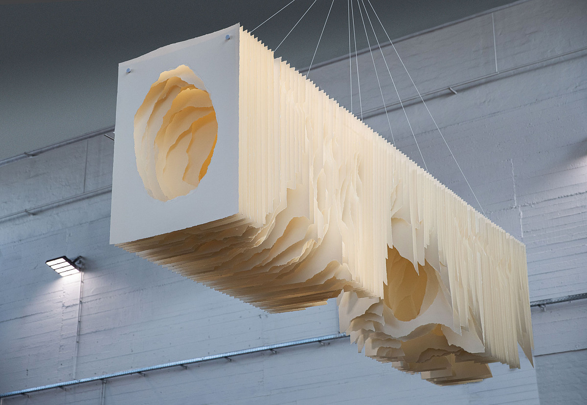 Einzelne, unterschiedlich eingerissene natur-farbene Papiere hängen nah aneinander gereiht von der Decke.
