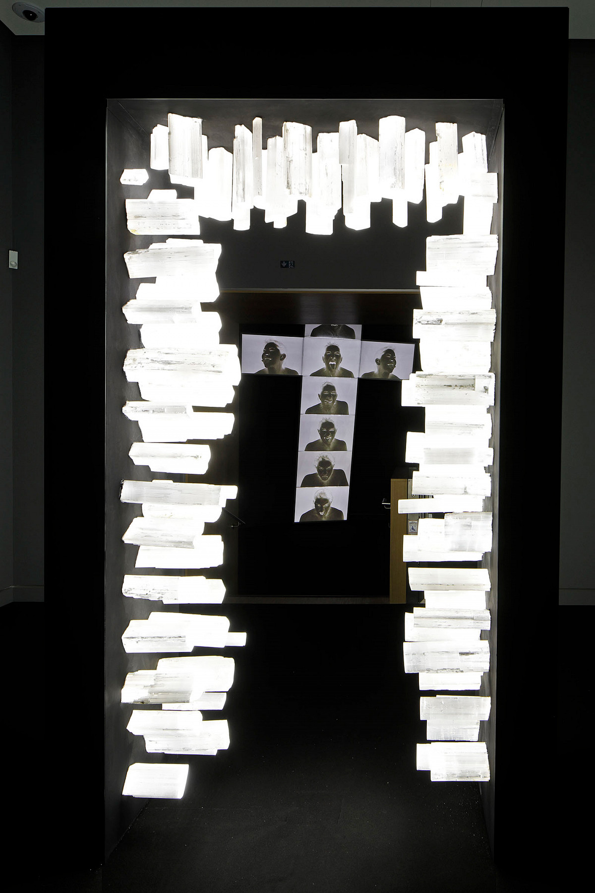 A door arch with glowing crystal blocks attached to its inner sides. Through the arch, you can see a cross on which several screens display a shadowy portrait.