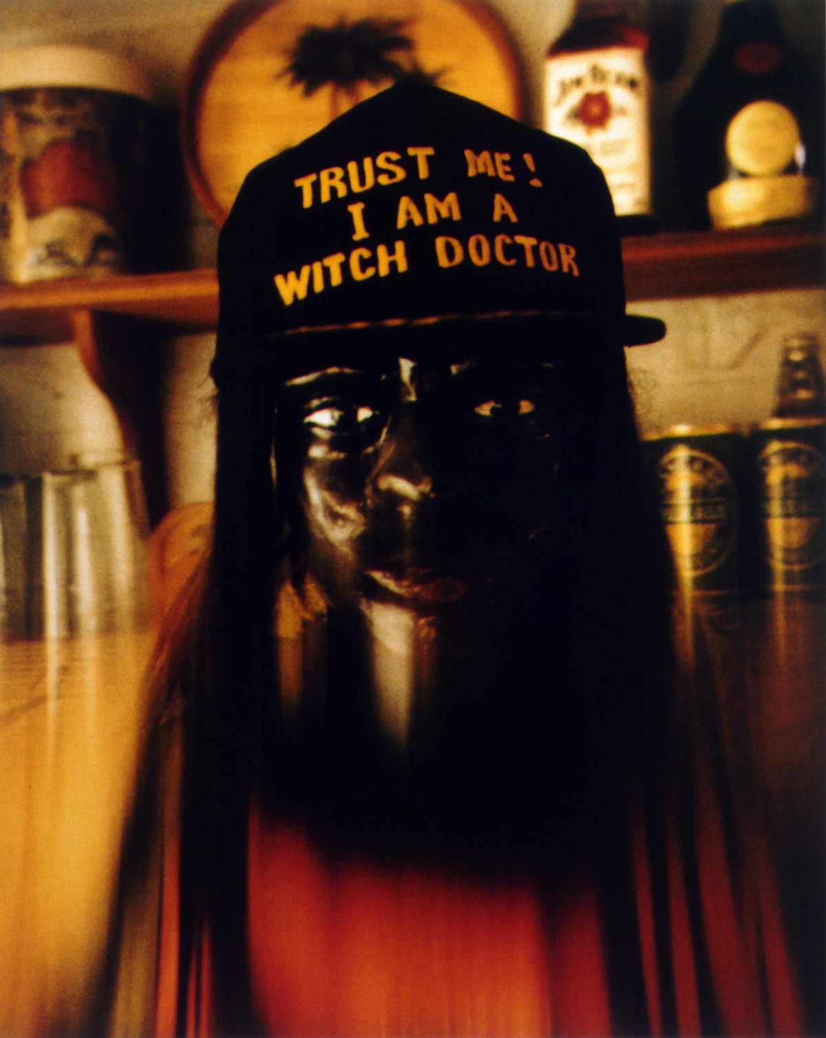 Fotografie einer Maske, die wie ein Gesicht aussieht, und eine Cap mit der Aufschrift ,,Trust me! I am a witch doctor'' trägt.