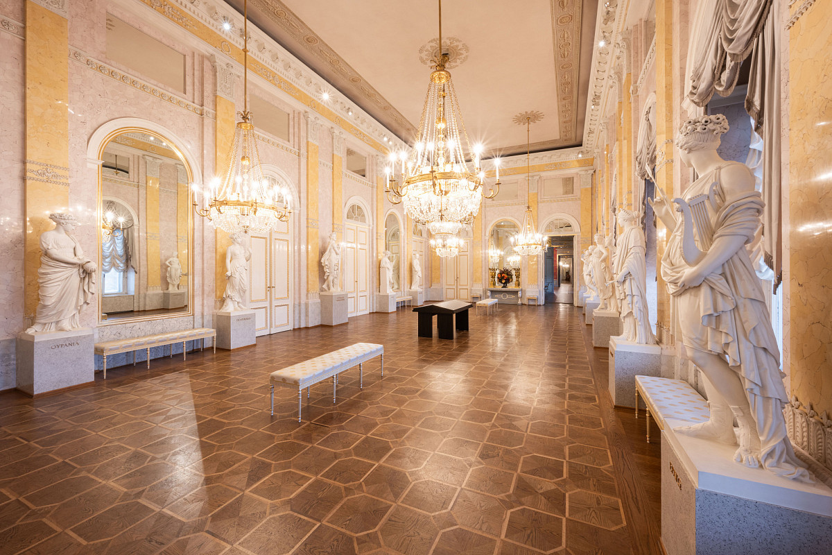 Photo of the Albertina museum's Muses Hall: historic ambience with parquet flooring and several chandeliers from the ceiling. Statues of muses on the walls.