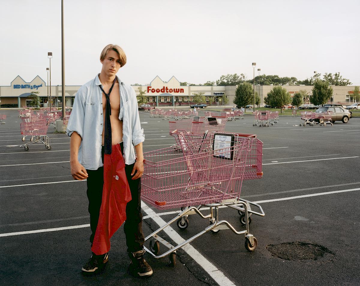 Joel Sternfeld: Young Man Gathering Shopping Carts, Huntington, New York from the series: Stranger Passing , July 1993